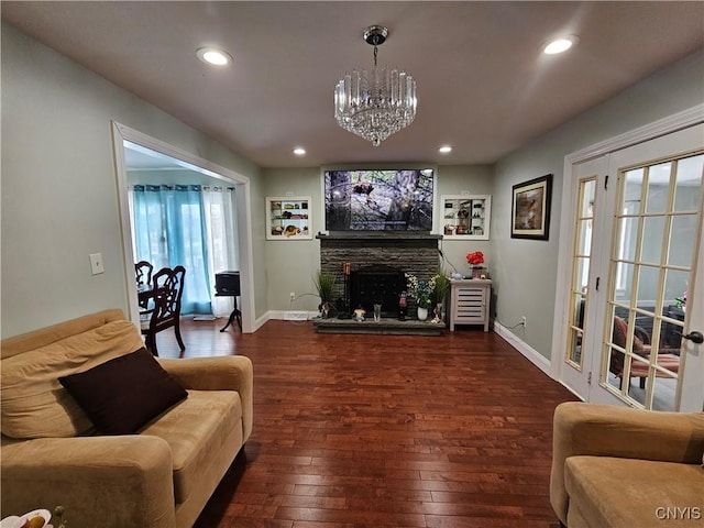 living room featuring dark wood-type flooring, a chandelier, and a stone fireplace