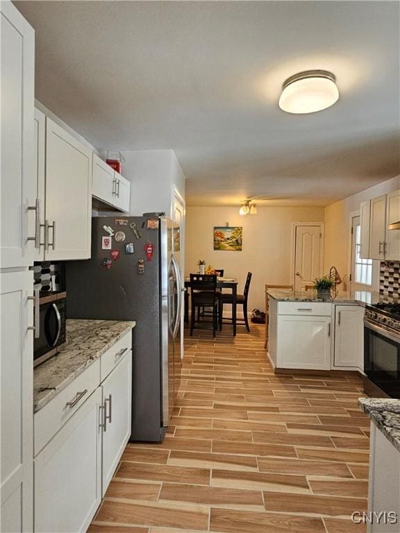 kitchen featuring light hardwood / wood-style floors, decorative backsplash, white cabinetry, light stone countertops, and stainless steel appliances