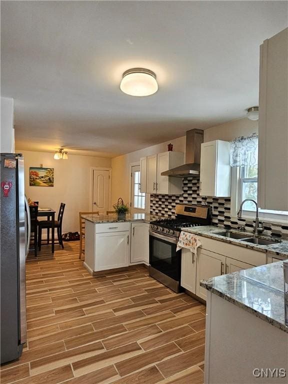 kitchen with white cabinets, kitchen peninsula, wall chimney range hood, and stainless steel appliances