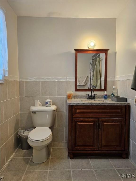 bathroom with tile walls, toilet, vanity, and tile patterned flooring