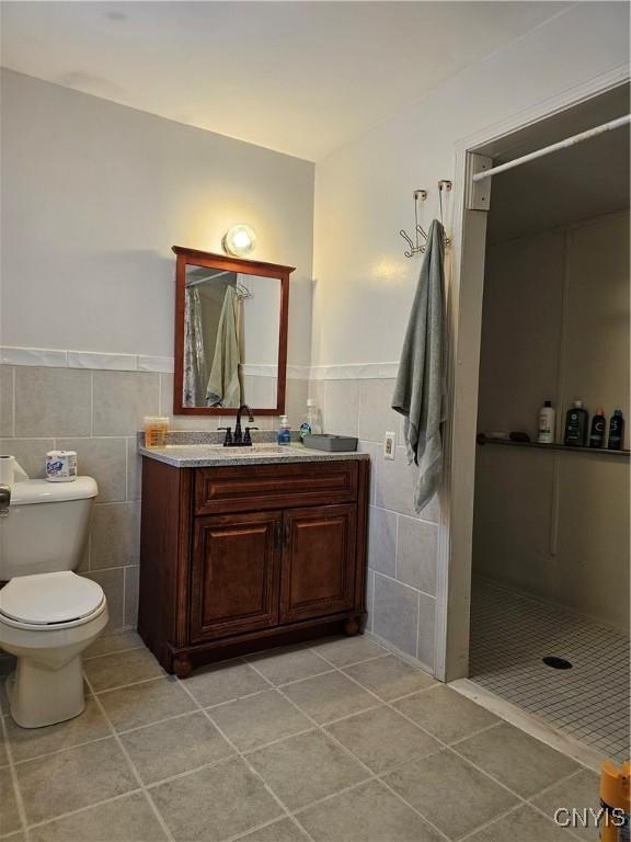 bathroom featuring toilet, tiled shower, tile patterned flooring, tile walls, and vanity