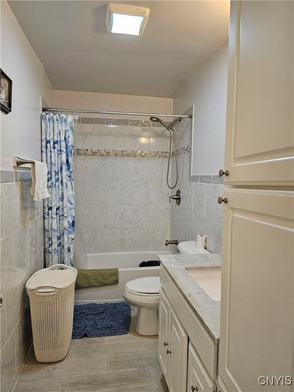 full bathroom featuring toilet, tile walls, shower / bath combo, and vanity