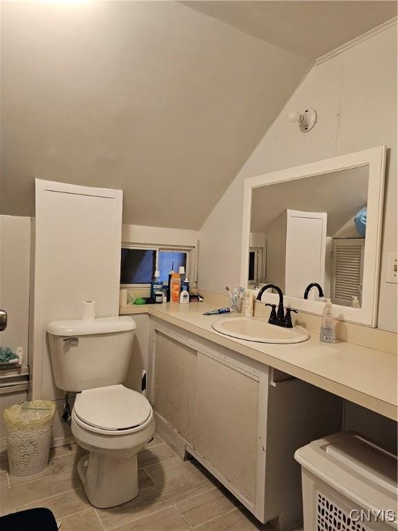 bathroom with toilet, vanity, and lofted ceiling