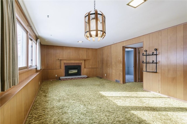 unfurnished living room featuring a brick fireplace, wooden walls, an inviting chandelier, and carpet flooring