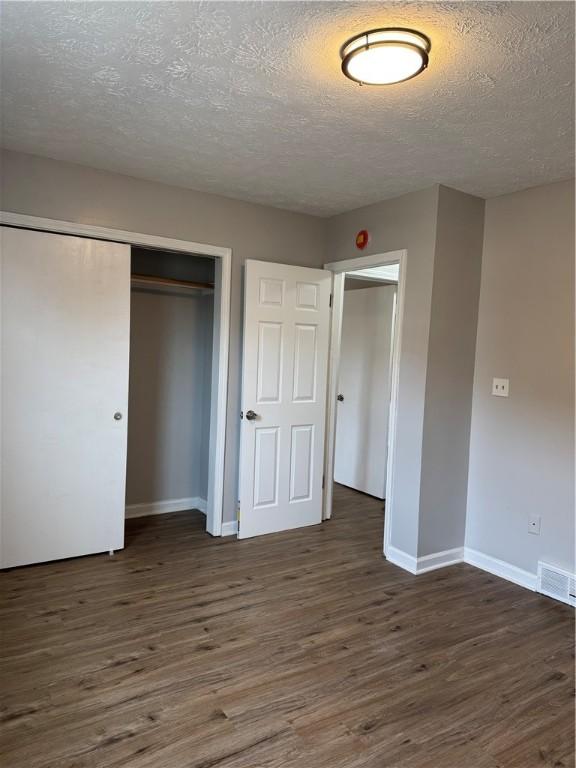 unfurnished bedroom with a closet, dark hardwood / wood-style flooring, and a textured ceiling