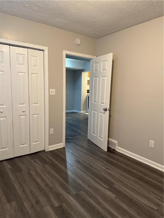 unfurnished bedroom featuring a textured ceiling, a closet, and dark hardwood / wood-style flooring