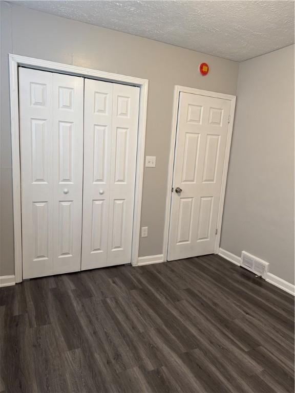 unfurnished bedroom featuring a closet, dark hardwood / wood-style floors, and a textured ceiling