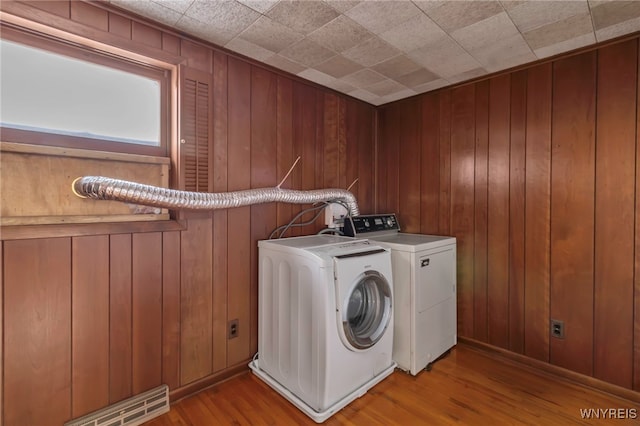 clothes washing area featuring washing machine and dryer, wooden walls, and light hardwood / wood-style flooring