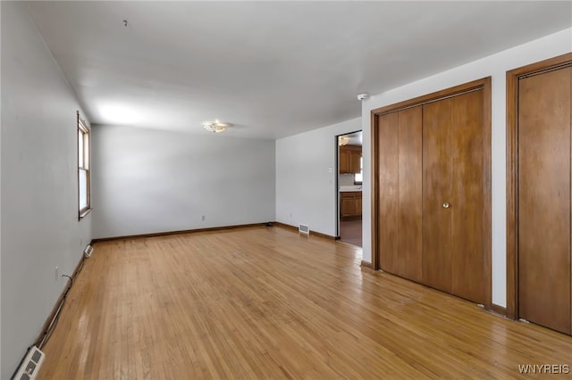 unfurnished bedroom with ensuite bathroom, two closets, and light hardwood / wood-style floors