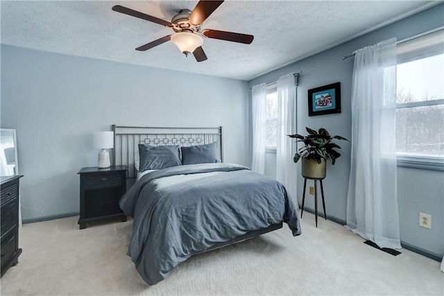 bedroom with ceiling fan, light colored carpet, and a textured ceiling