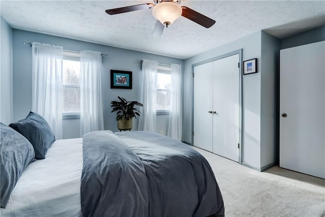 carpeted bedroom featuring ceiling fan, a closet, a textured ceiling, and multiple windows