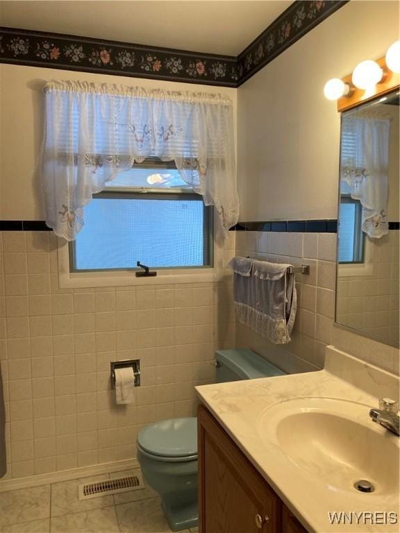 bathroom with toilet, tile patterned flooring, tile walls, and vanity