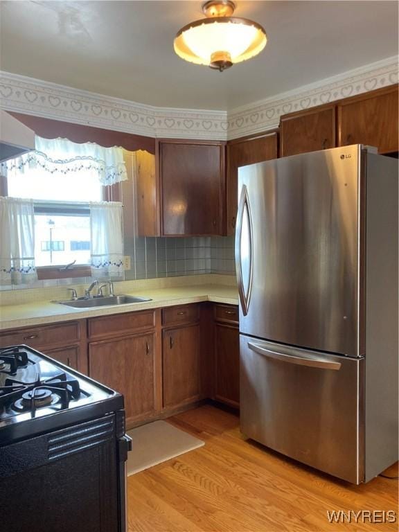 kitchen with backsplash, black range with gas stovetop, sink, stainless steel refrigerator, and light wood-type flooring