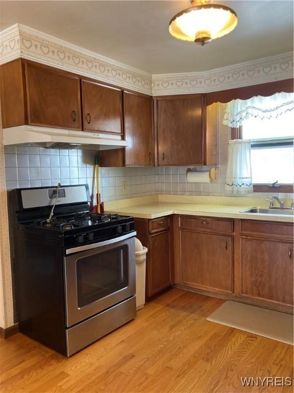 kitchen with sink, stainless steel range with gas stovetop, decorative backsplash, and light hardwood / wood-style floors