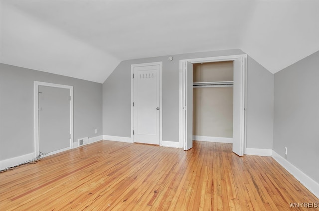 unfurnished bedroom featuring multiple closets, vaulted ceiling, and light hardwood / wood-style floors