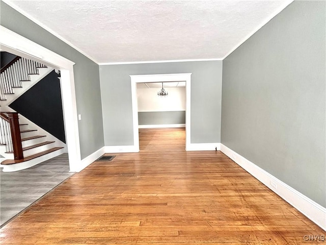 unfurnished room featuring hardwood / wood-style floors, ornamental molding, a textured ceiling, and an inviting chandelier