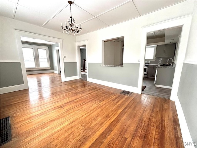 unfurnished living room featuring hardwood / wood-style flooring, sink, and an inviting chandelier