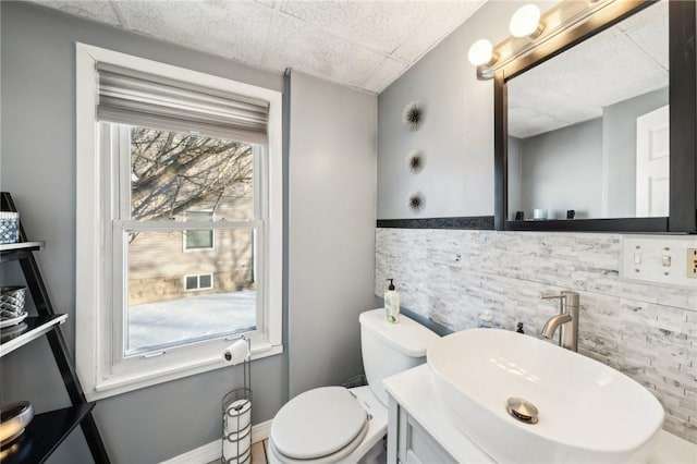 bathroom featuring toilet, vanity, a paneled ceiling, and a wealth of natural light