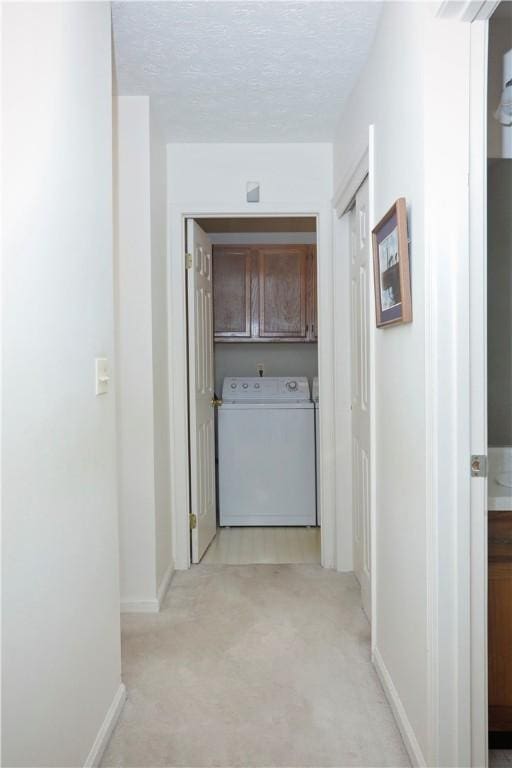 corridor featuring light carpet, washer / clothes dryer, and a textured ceiling