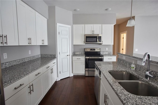 kitchen featuring white cabinets, stainless steel appliances, dark stone countertops, sink, and hanging light fixtures