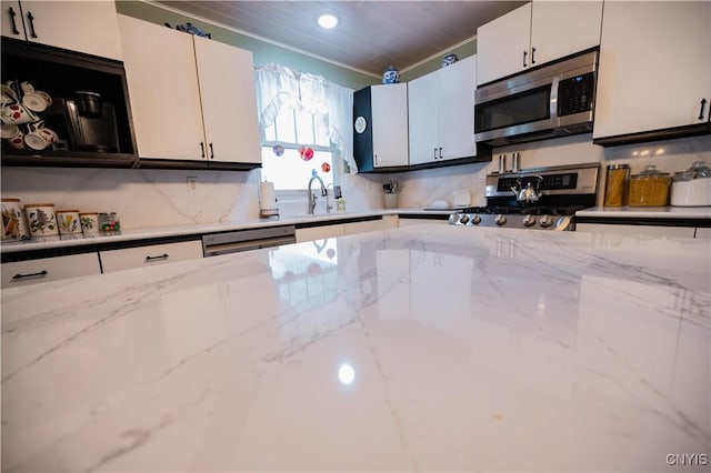 kitchen featuring white cabinets, appliances with stainless steel finishes, light stone counters, a sink, and backsplash