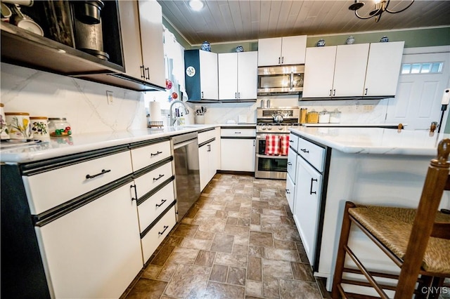 kitchen featuring white cabinets, appliances with stainless steel finishes, wood ceiling, a kitchen breakfast bar, and sink