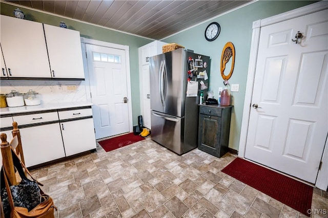 kitchen featuring stone finish floor, freestanding refrigerator, light countertops, and white cabinets