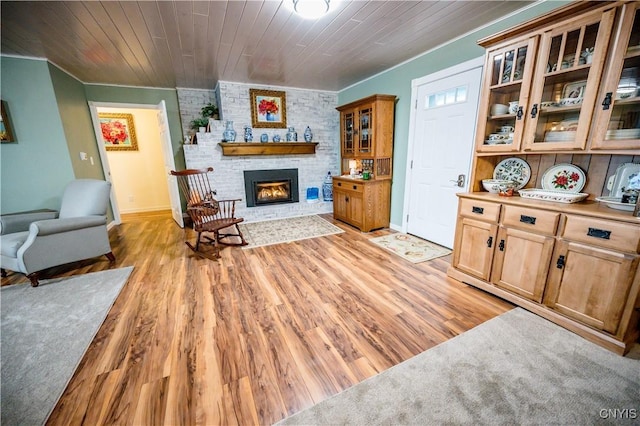 living room featuring a brick fireplace, wooden ceiling, ornamental molding, and light wood-type flooring