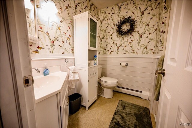 bathroom with toilet, a baseboard radiator, vanity, wainscoting, and wallpapered walls