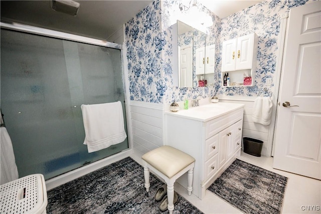 bathroom featuring a stall shower, wallpapered walls, vanity, and a wainscoted wall