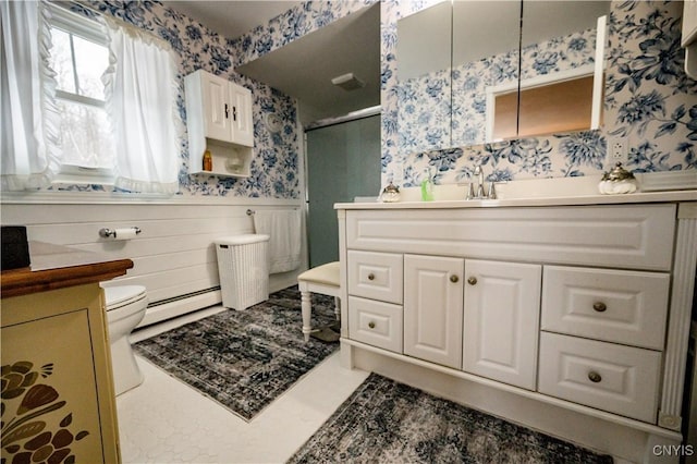 full bath featuring baseboard heating, wallpapered walls, vanity, and wainscoting