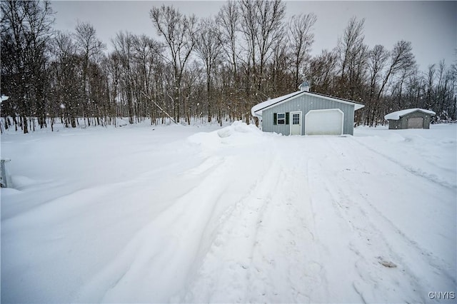 snowy yard with a garage and an outbuilding