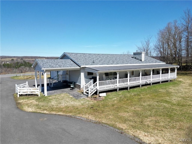 view of front facade featuring a carport, covered porch, a chimney, a front lawn, and roof with shingles