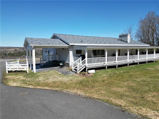 view of front of home featuring a front yard, a carport, a porch, a chimney, and roof with shingles