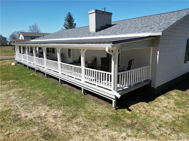 rear view of property featuring a shingled roof, a chimney, and a lawn