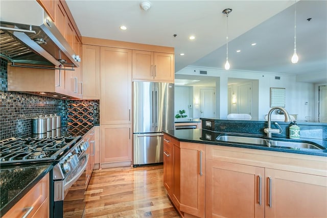 kitchen featuring stainless steel appliances, dark stone counters, range hood, pendant lighting, and sink