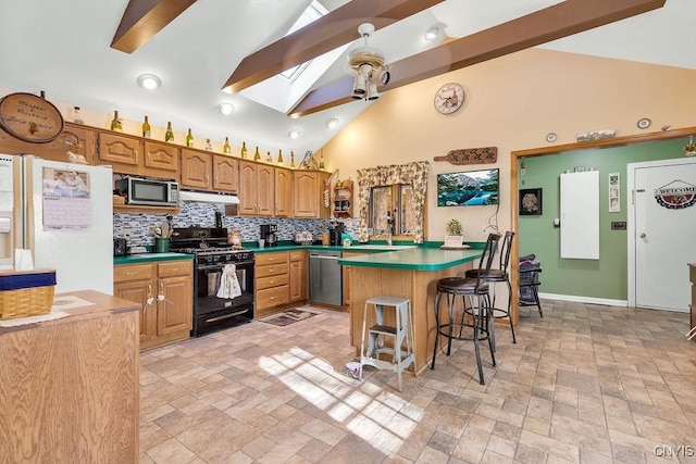 kitchen featuring backsplash, a skylight, appliances with stainless steel finishes, a kitchen breakfast bar, and high vaulted ceiling