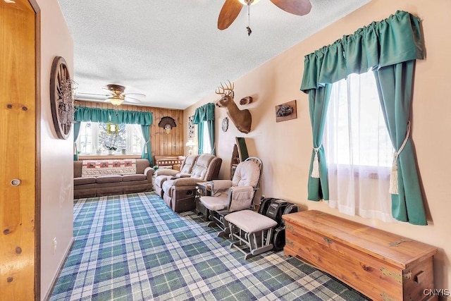 sitting room with ceiling fan, wood walls, and a textured ceiling