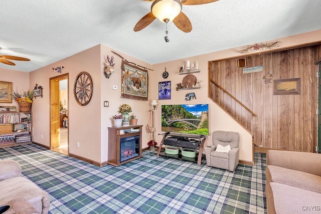 living room with a textured ceiling, ceiling fan, dark carpet, and wooden walls