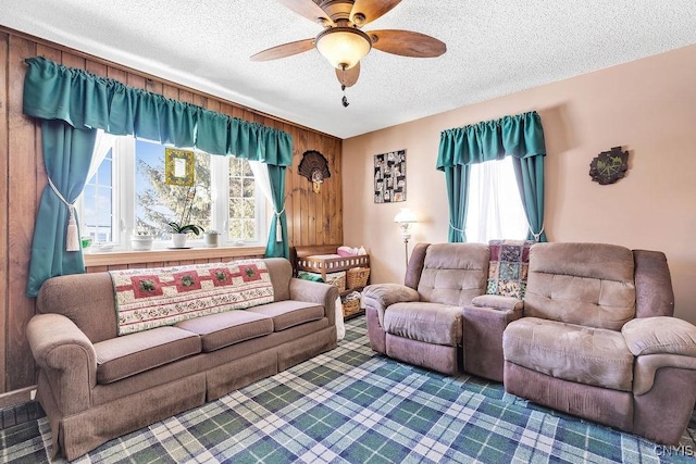 living room featuring ceiling fan, plenty of natural light, a textured ceiling, and wood walls