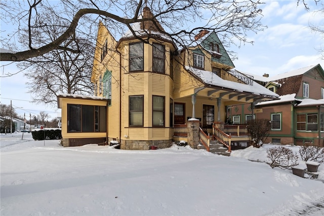 snow covered rear of property featuring covered porch