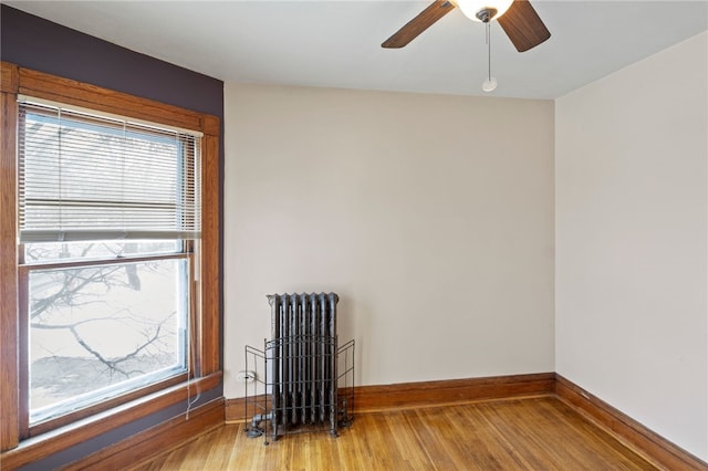 empty room featuring ceiling fan, radiator heating unit, light hardwood / wood-style floors, and plenty of natural light