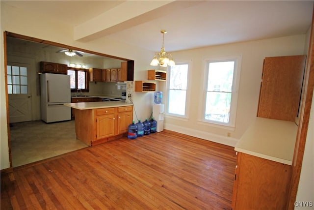 kitchen featuring hanging light fixtures, white fridge, light wood-type flooring, beam ceiling, and kitchen peninsula