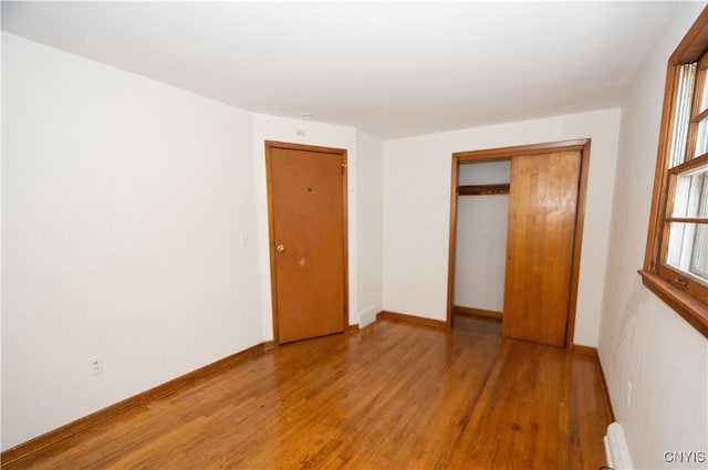 unfurnished bedroom with wood-type flooring, a baseboard radiator, and a closet