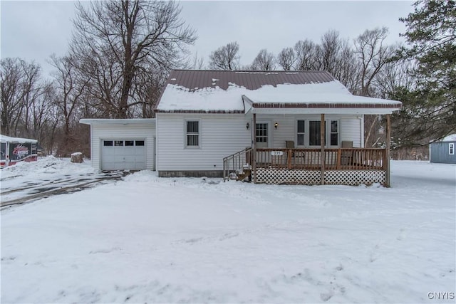 snow covered property with a garage, an outbuilding, and a porch