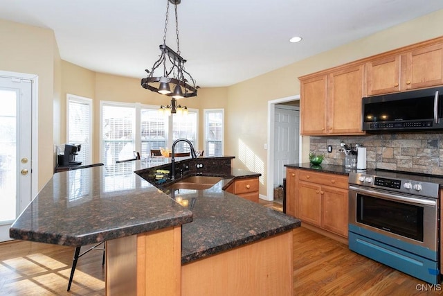 kitchen with light hardwood / wood-style floors, stainless steel electric range oven, hanging light fixtures, a kitchen island with sink, and sink