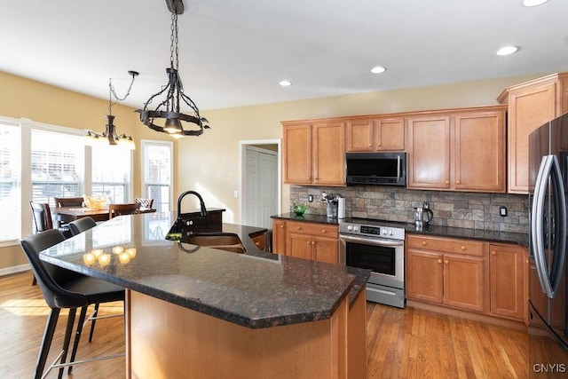 kitchen with backsplash, a kitchen island with sink, hanging light fixtures, and stainless steel appliances