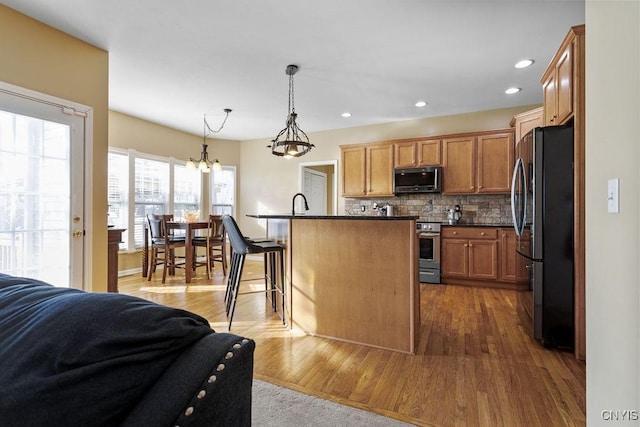 kitchen with black refrigerator, tasteful backsplash, an island with sink, hanging light fixtures, and a breakfast bar area