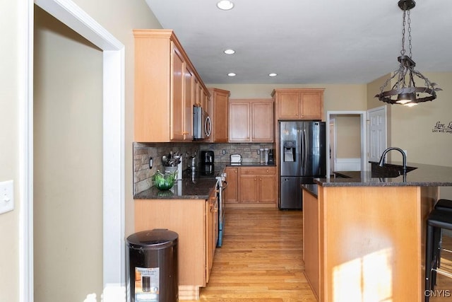 kitchen featuring stainless steel appliances, sink, backsplash, hanging light fixtures, and light wood-type flooring