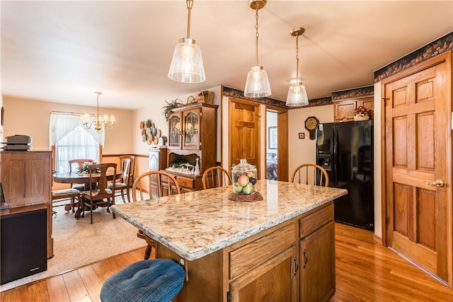 kitchen with pendant lighting, a center island, light wood-type flooring, light stone counters, and black fridge with ice dispenser